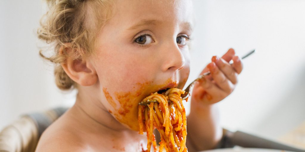 Young toddler boy eating messy pasta